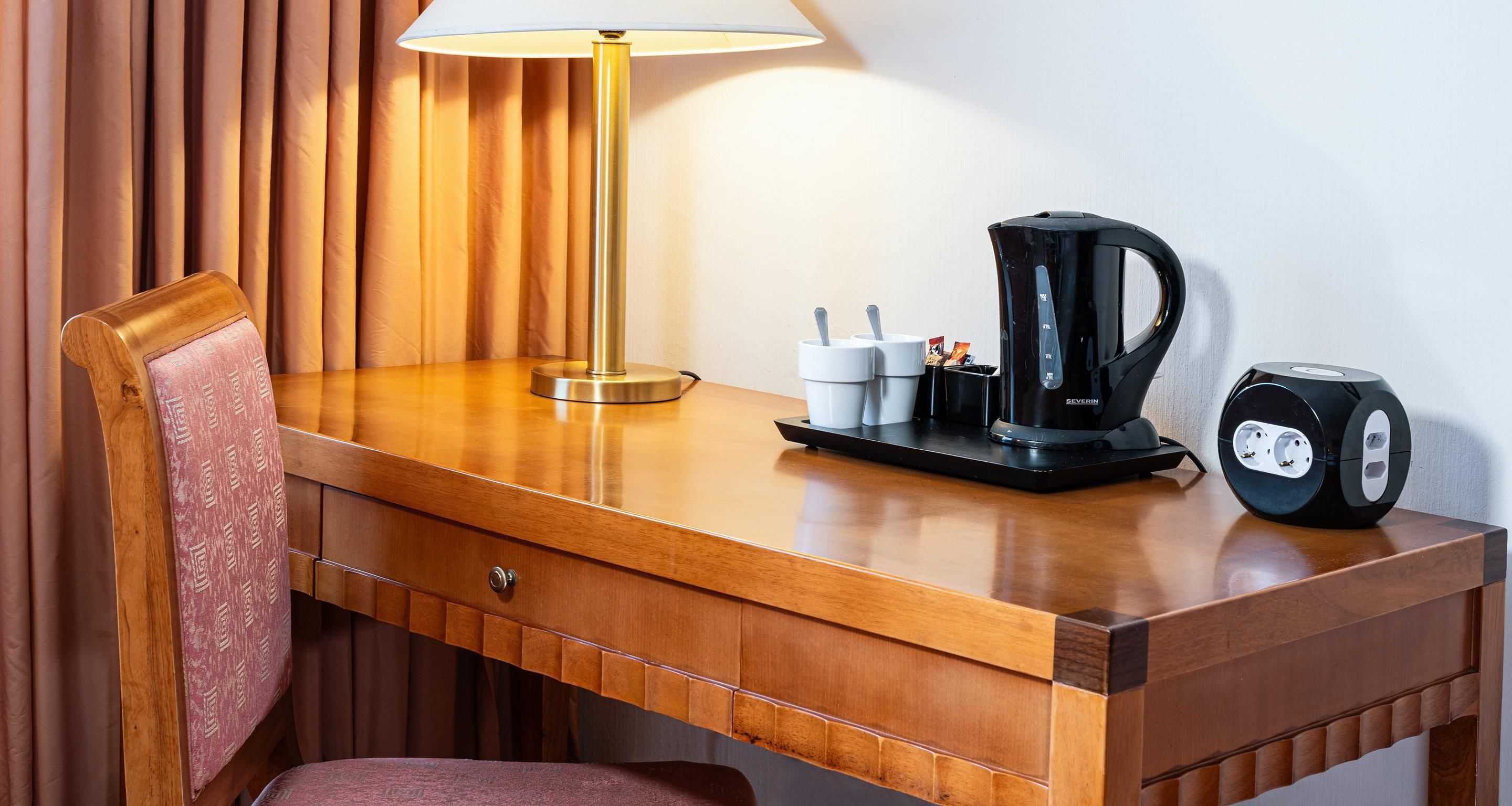 A wooden desk with a lamp, a coffee maker, and a clock.
