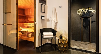 Un baño moderno con sauna de madera, una silla negra con una toalla, un florero dorado y una planta en maceta.