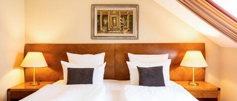 Habitación de hotel con una cama grande, dos mesitas de noche con lámparas, un cuadro enmarcado en la pared y un cabecero de madera.