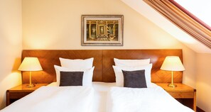 Habitación de hotel con una cama grande, dos mesitas de noche con lámparas, un cuadro enmarcado en la pared y un cabecero de madera.