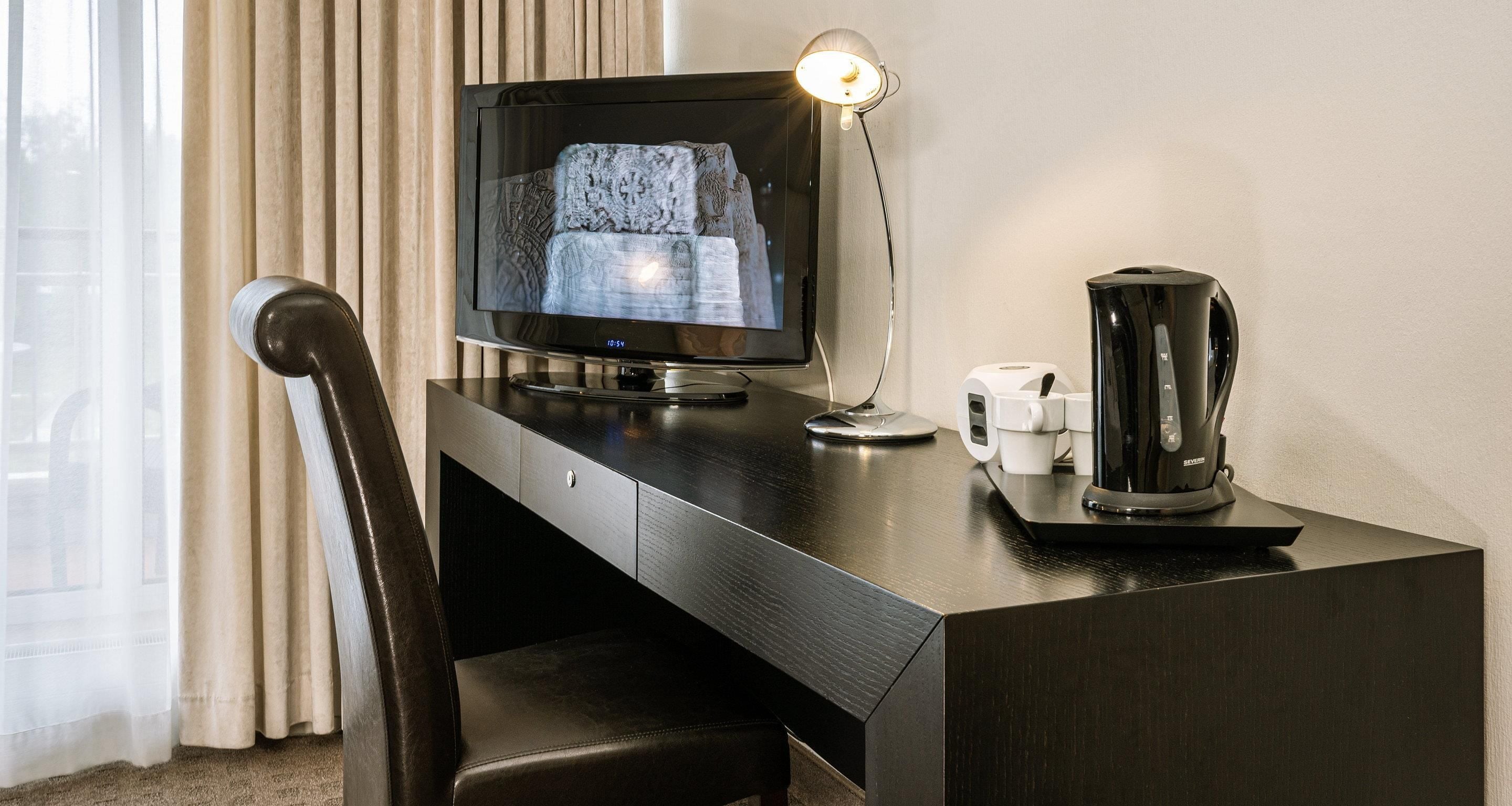 Een hotelkamer met een donker houten bureau, een televisie, een koffiezetapparaat en een stoel.