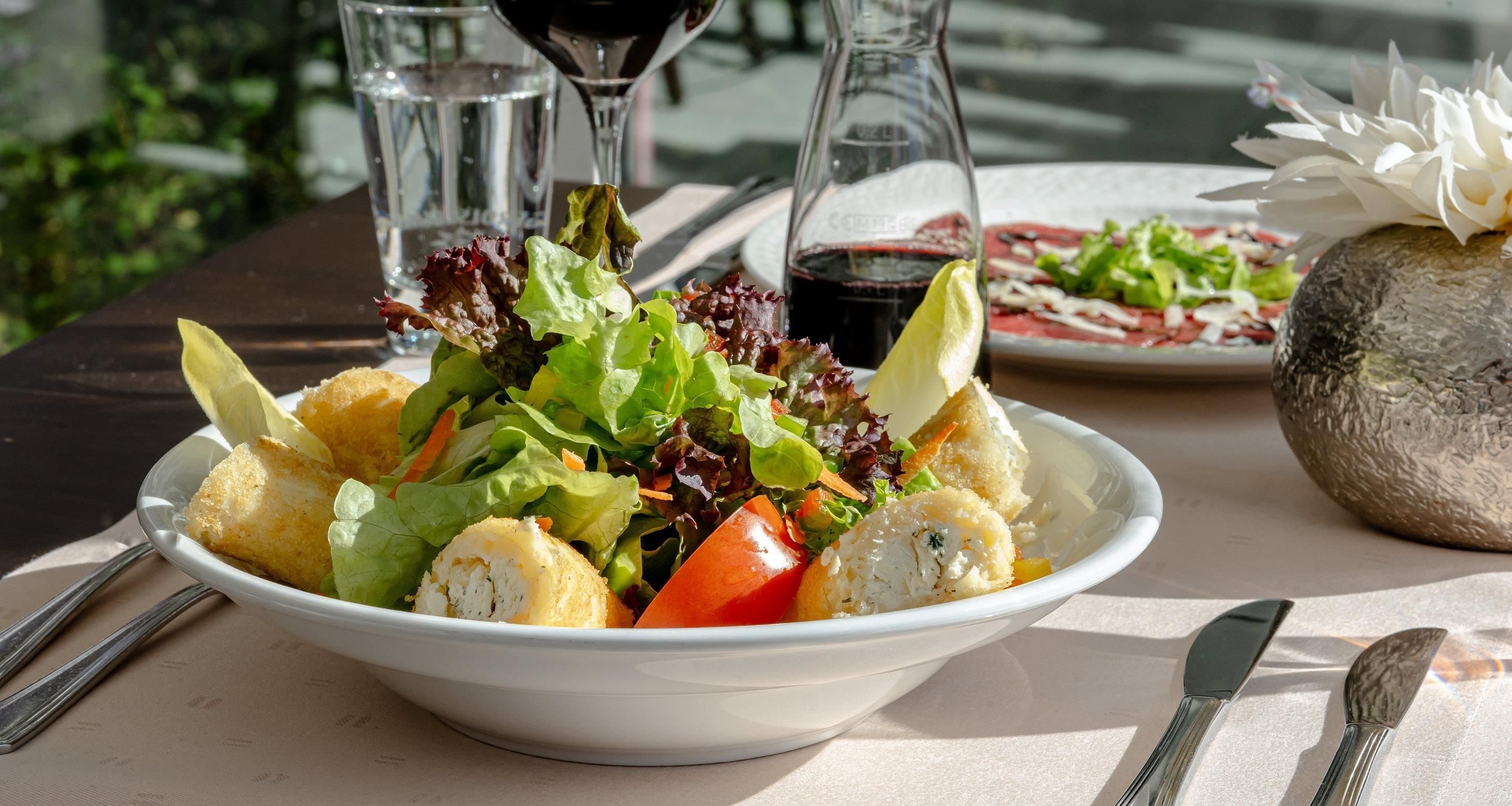 Ein Tisch mit einer Salatschüssel, einer Weinflasche und einem Teller mit Essen.