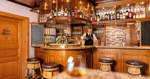 A bar area with a bartender, wooden bar counter, stools, and a variety of bottles.