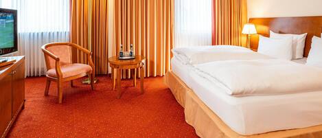 A hotel room with a bed, a chair, a small table with a tray, a TV, and curtains.