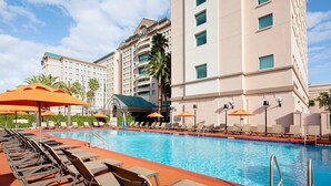 A hotel pool area with sun loungers and umbrellas, a clear blue pool, and a multi-story building in the background. - Florida Hotel & Conference Center in the Florida Mall (Orlando)