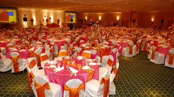 Un amplio salón de banquetes con mesas redondas cubiertas con manteles rosas y sillas blancas adornadas con cintas anaranjadas.