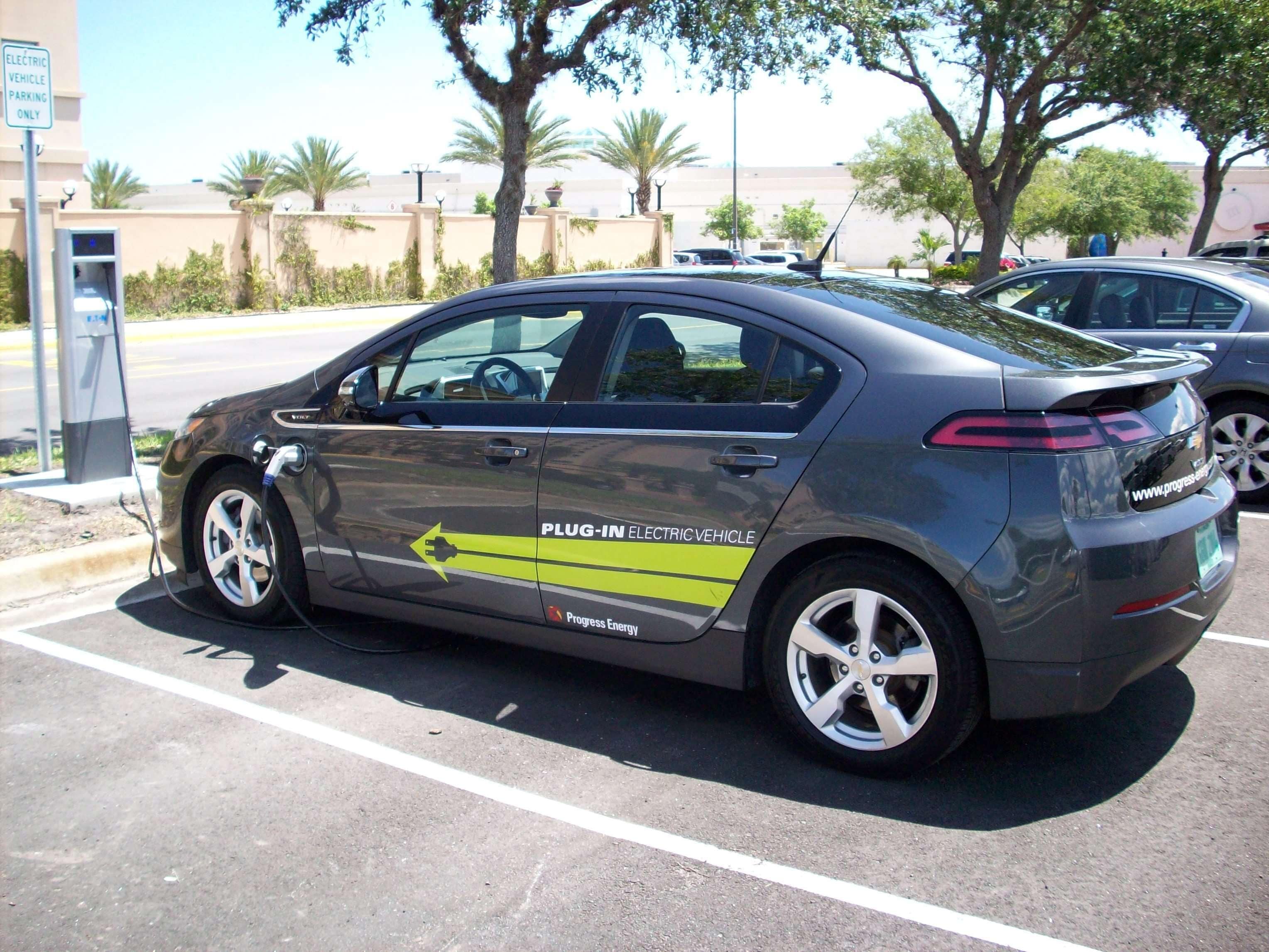 A gray electric vehicle charging at a station with a Progress Energy logo.