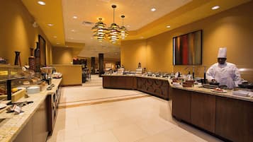 A hotel kitchen with a buffet setup, a chef preparing food, and a modern interior design.