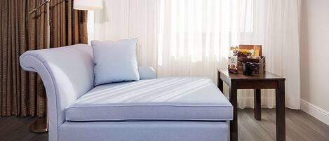 Una habitación de hotel moderna con una cama grande, una mesita con una lámpara y cortinas.