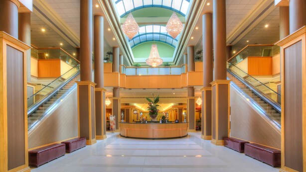A spacious lobby with a central reception desk, two escalators, and a high ceiling with large chandeliers. - Florida Hotel & Conference Center in the Florida Mall (Orlando)
