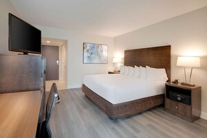 A hotel room with a large bed, bedside tables, a flat-screen TV, and a painting on the wall.