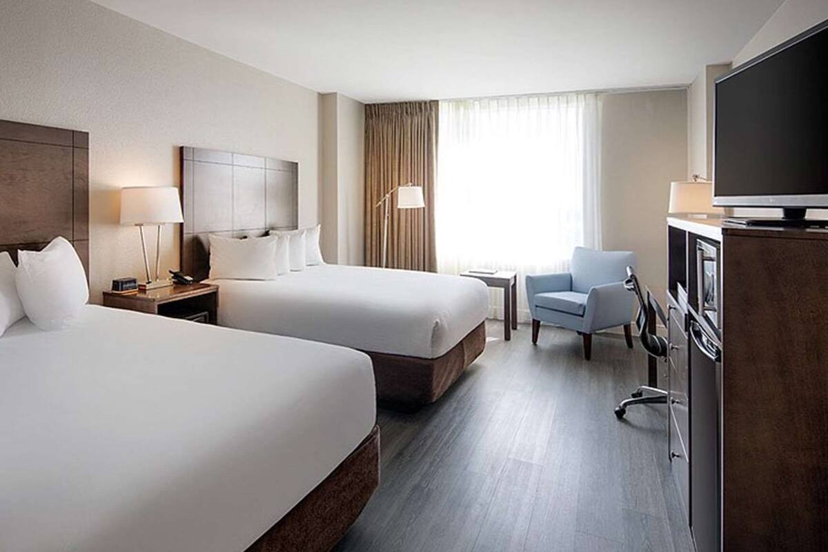 A hotel room with two beds, a TV, a desk, a chair, and a window with curtains.