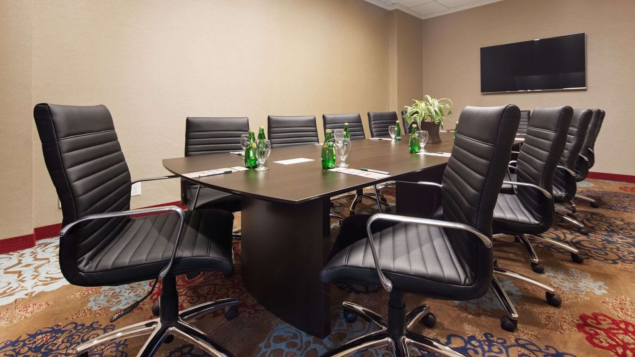 A conference room with a large table, black leather chairs, and a television on the wall.