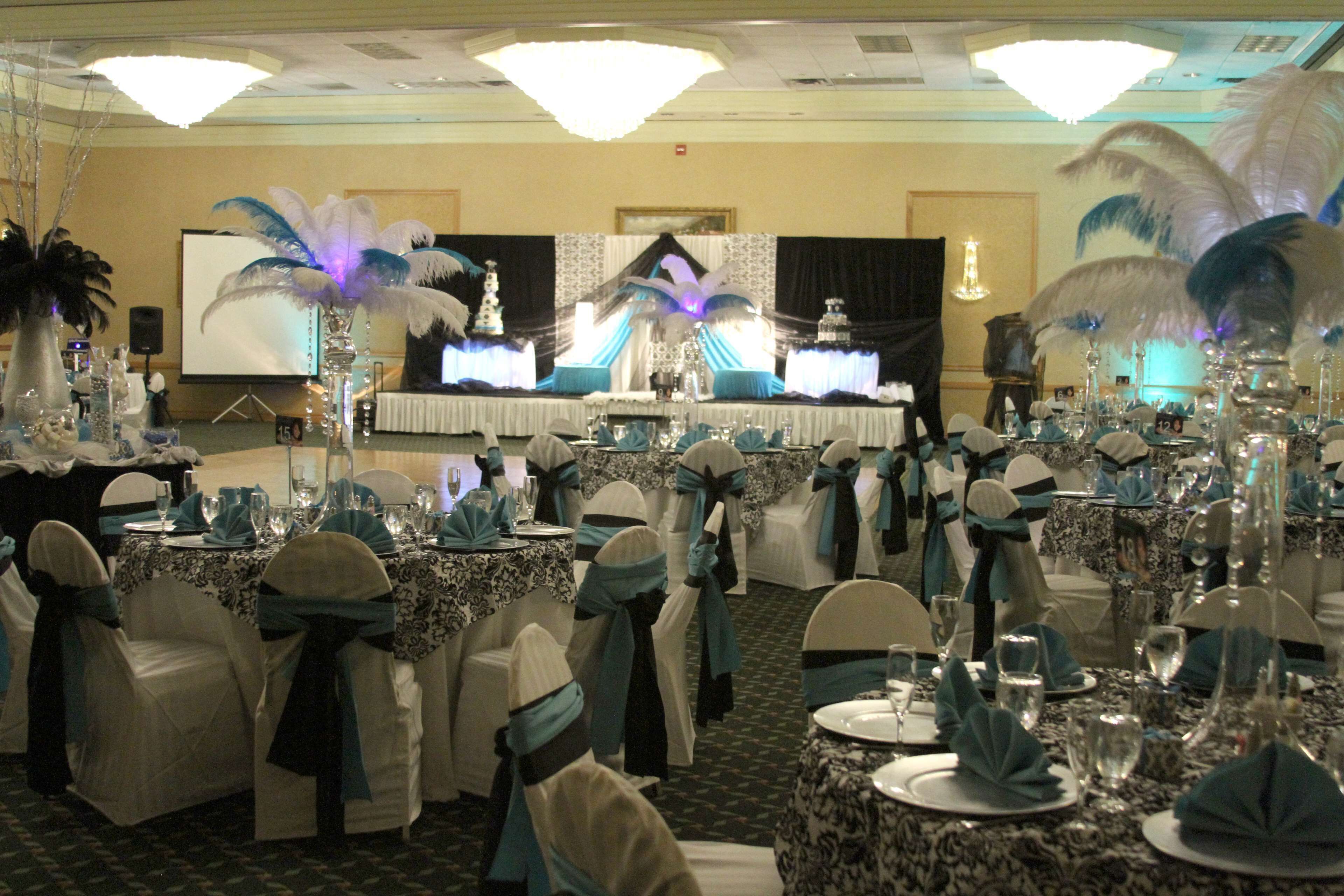 A banquet hall with round tables set for a formal event, featuring white and blue decor and feathered centerpieces.
