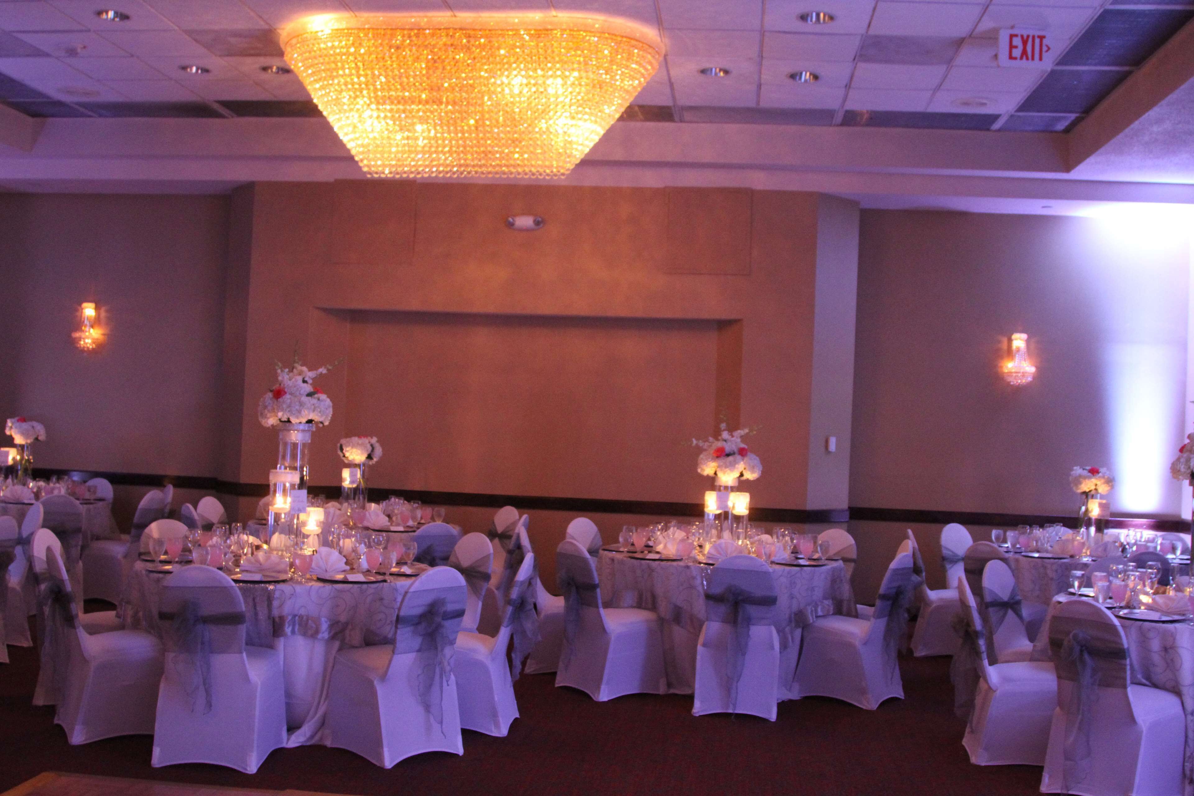 Une salle de banquet avec des tables rondes dressées pour un événement formel, agrémentée de nappes blanches et de centres de table floraux.