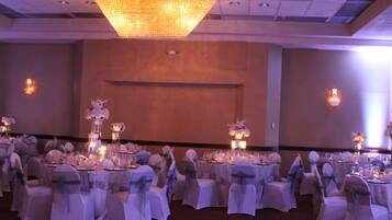 Un salón de banquetes con mesas redondas dispuestas para un evento formal, con manteles blancos y centros de mesa florales.