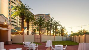 An outdoor patio area with tables and chairs, palm trees, and string lights. - Florida Hotel & Conference Center in the Florida Mall (Orlando)