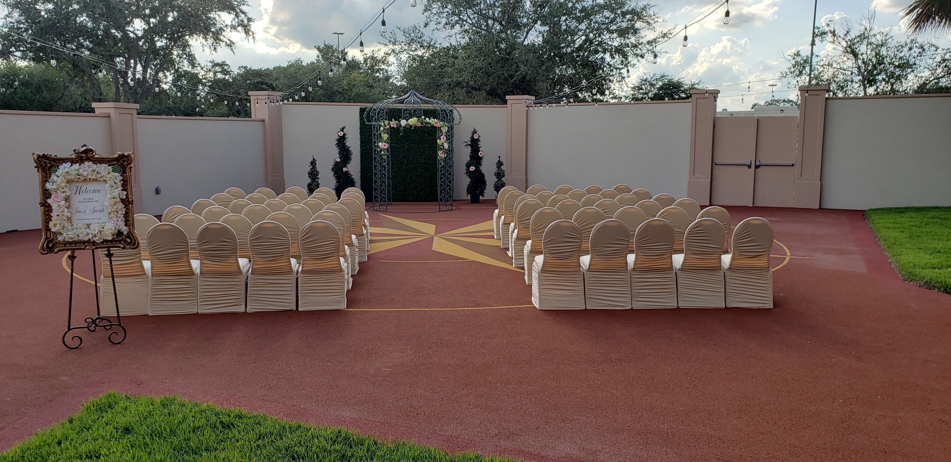 Salón de bodas al aire libre con filas de sillas y un arco decorativo.