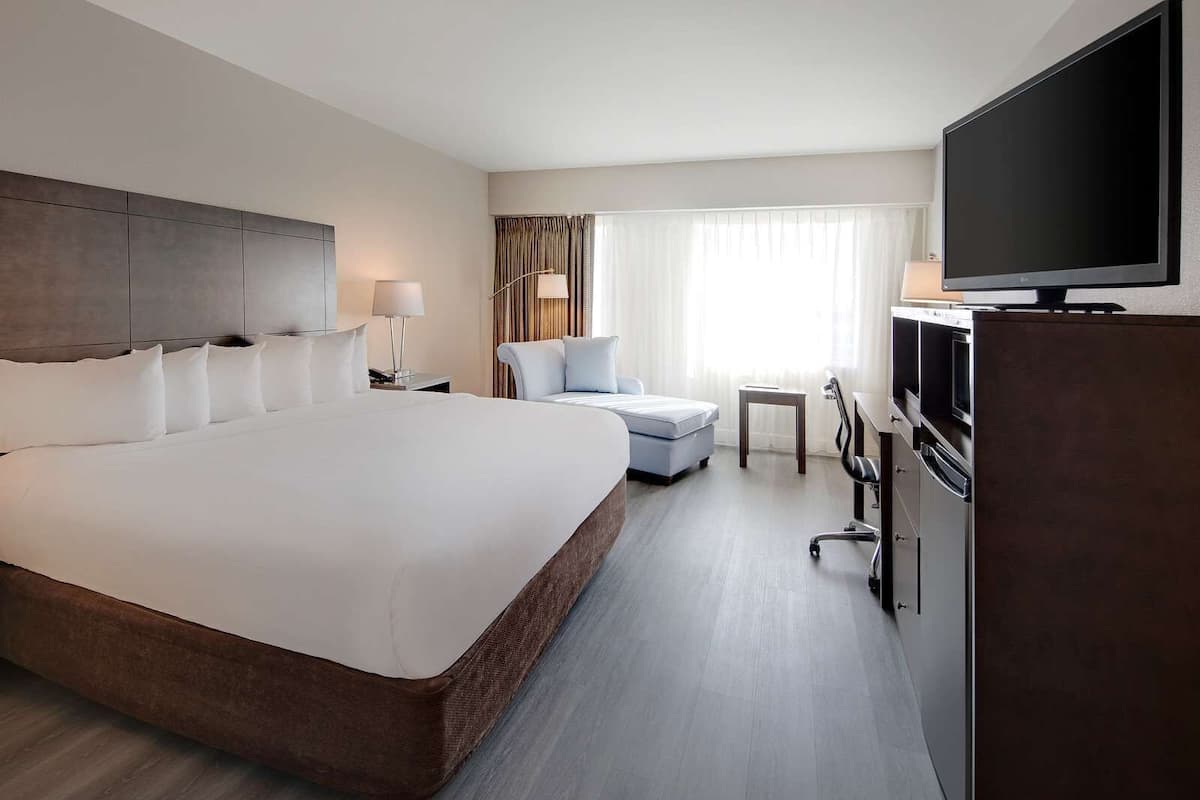 A hotel room with a large bed, a desk, a chair, a television, and a minibar.