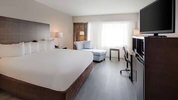 Ein Hotelzimmer mit einem großen Bett, einem Schreibtisch, einem Sessel, einem Fernseher und einer Minibar.