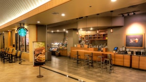 A Starbucks coffee shop with a counter, bar stools, and a seating area with tables and chairs. - Florida Hotel & Conference Center in the Florida Mall (Orlando)