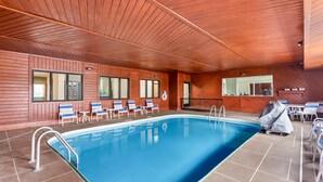 Piscina interior com teto e paredes de madeira, rodeada por espreguiçadeiras e uma área de estar coberta.