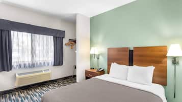 Habitación de hotel con una cama grande, una mesita de noche, una lámpara, un calefactor y una ventana con cortinas.