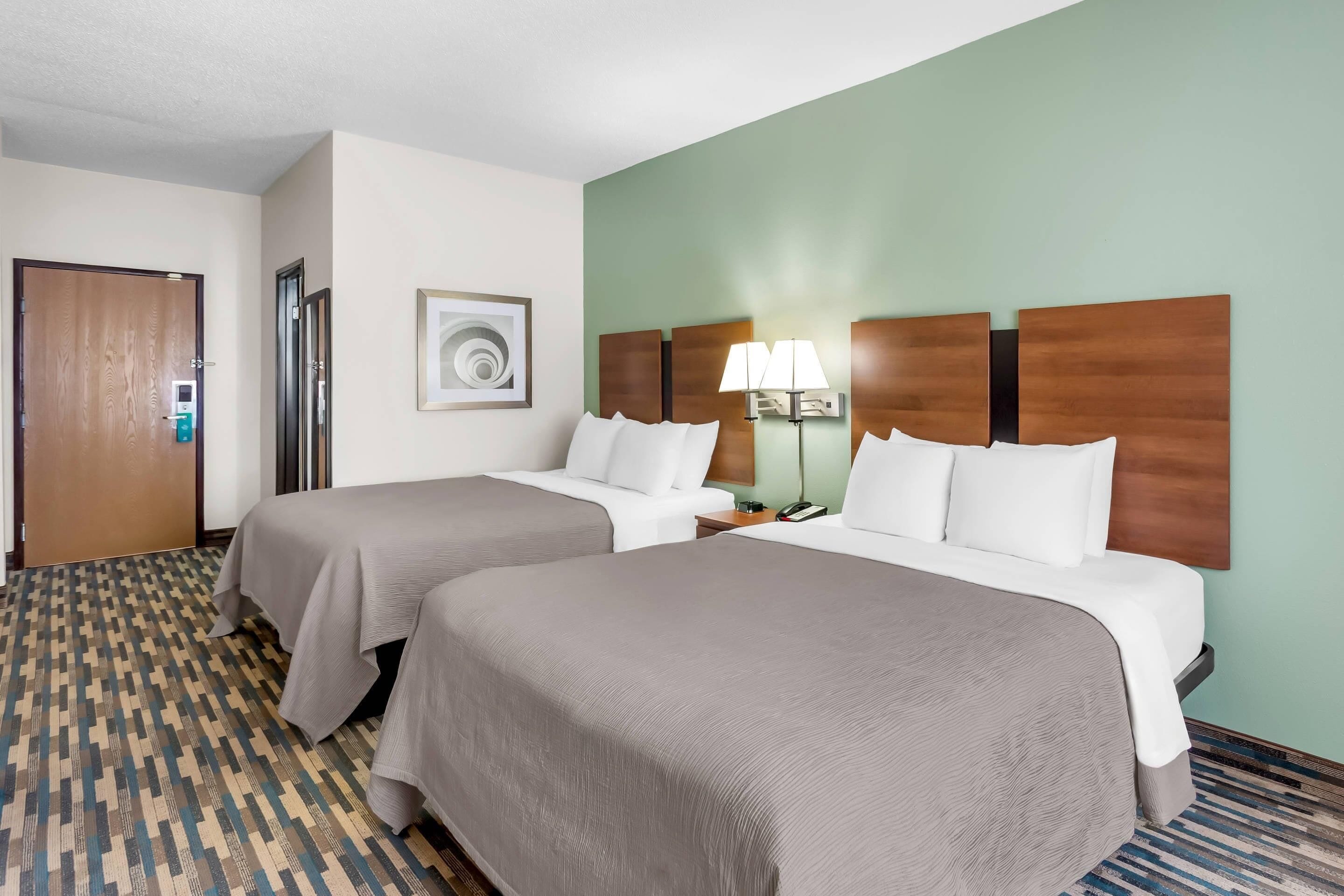 Una habitación de hotel con dos camas, una puerta, una lámpara de pared y una alfombra estampada.