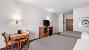 Quarto de hotel com cama, escrivaninha com cadeira, televisão e micro-ondas.