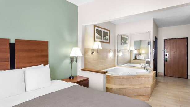 Quarto de hotel com uma cama grande, banheiro com banheira e cabeceira de madeira.