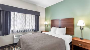 A hotel room with a large bed, two bedside tables with lamps, a heater, and a window with curtains.