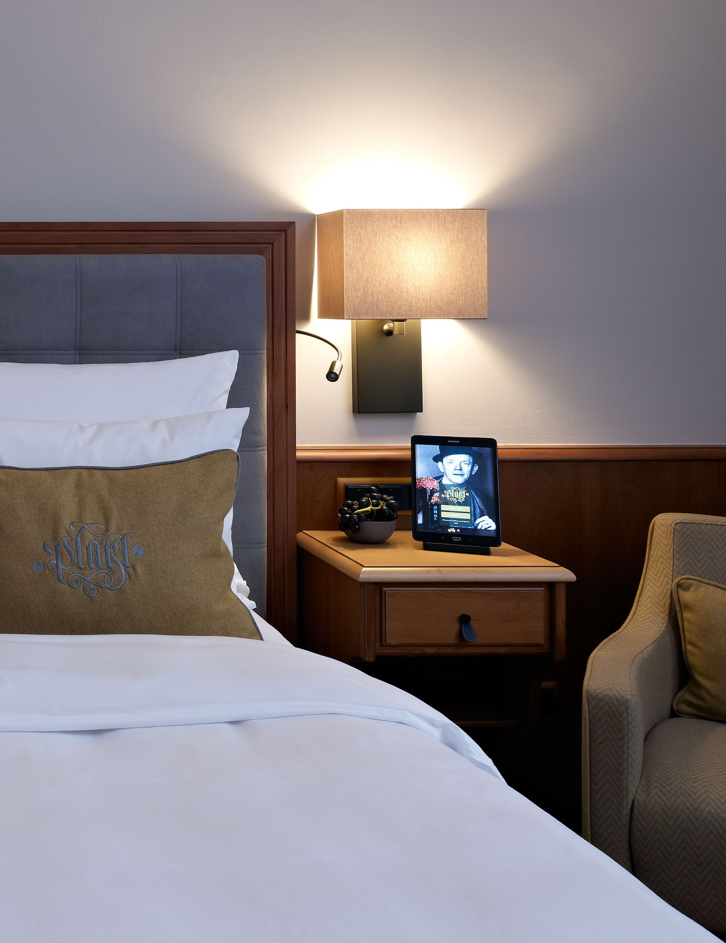 A hotel room with a bed, a bedside table with a lamp, a TV, and a chair.