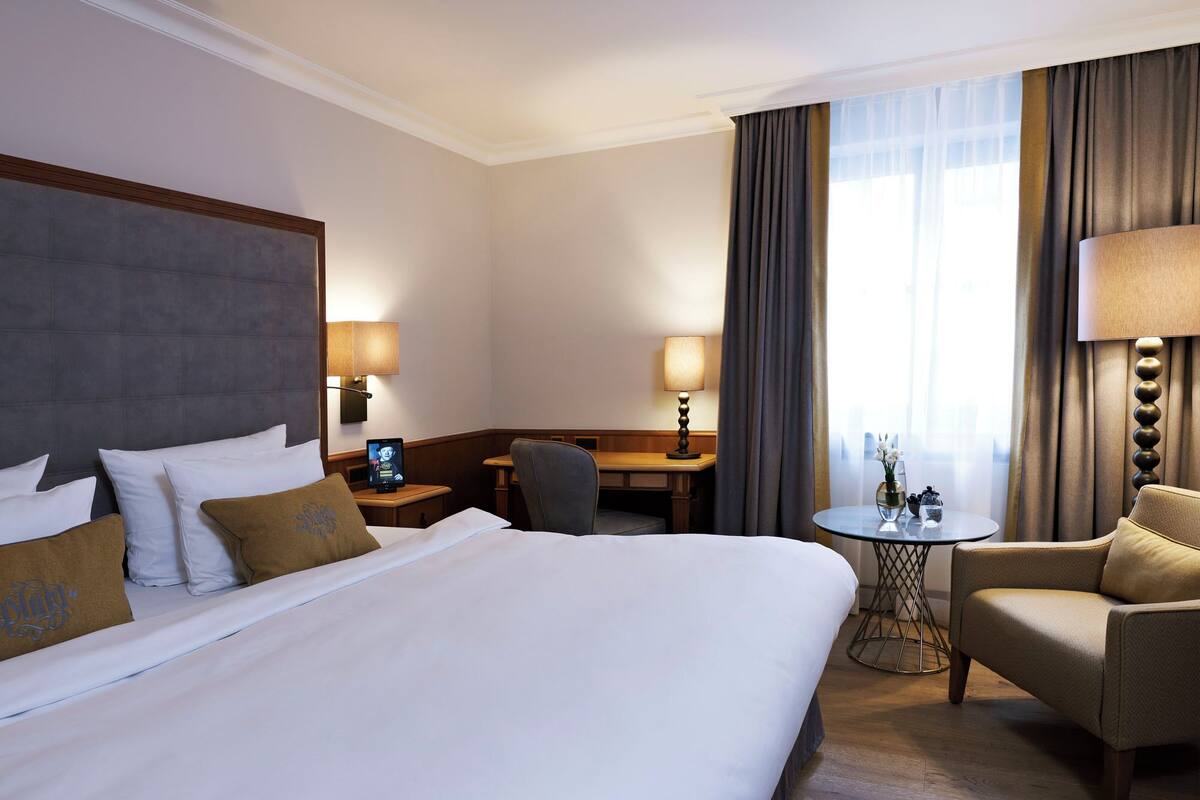 Habitación de hotel con una cama grande, un escritorio, una silla y una mesita de noche con lámpara.