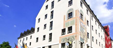 Un edificio histórico de varios pisos, con un reloj destacado y un mural en la fachada.