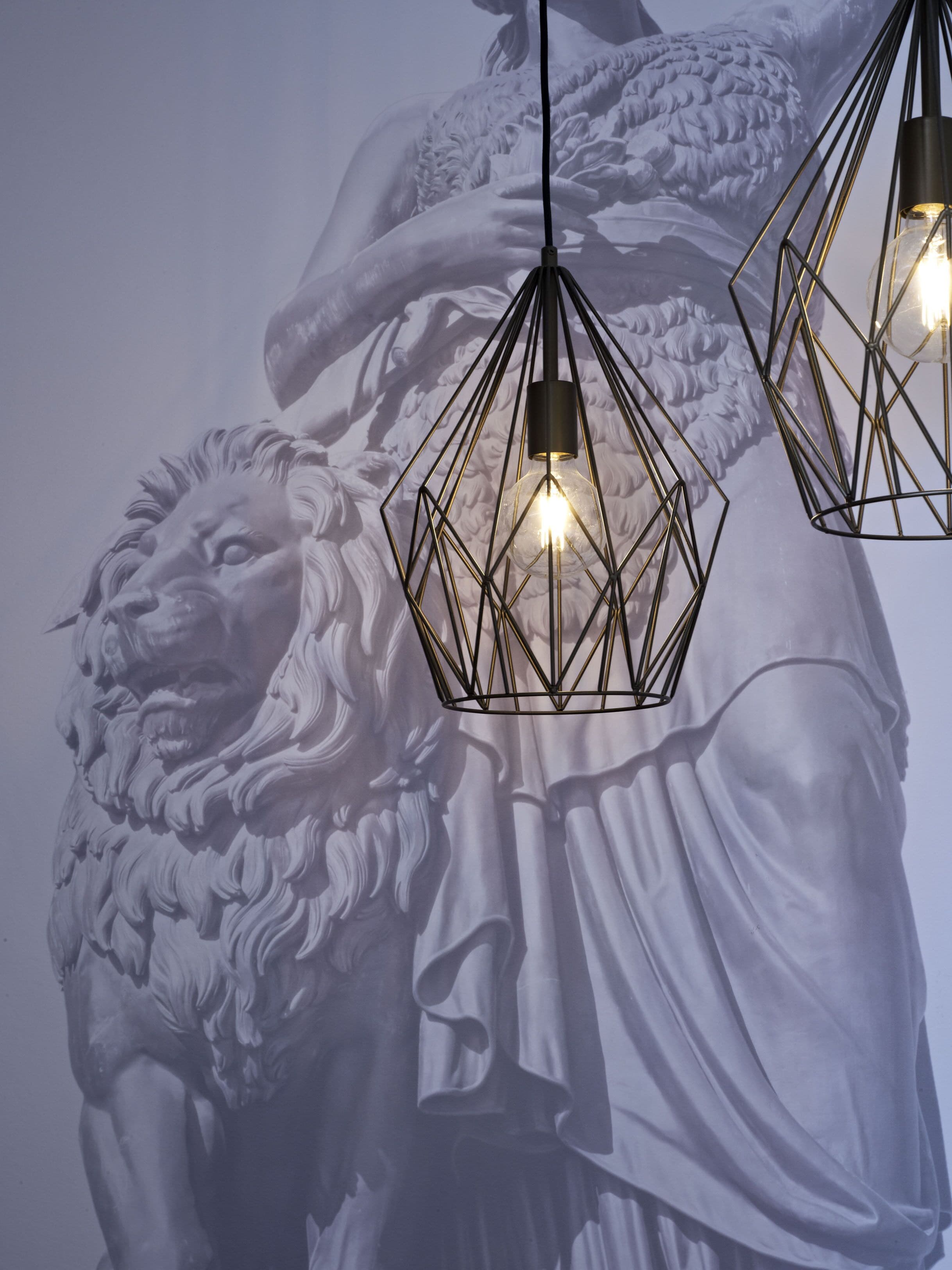 A statue with a lion's head and a draped garment, illuminated by geometric pendant lights.