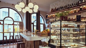 A bar area with stools, a display case with pastries, and a wine rack. - Platzl Hotel (Munich)