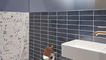 Ein Badezimmer mit einem weißen Waschbecken, dunkelblauen Fliesenwänden und einer Toilette mit Toilettenpapier.