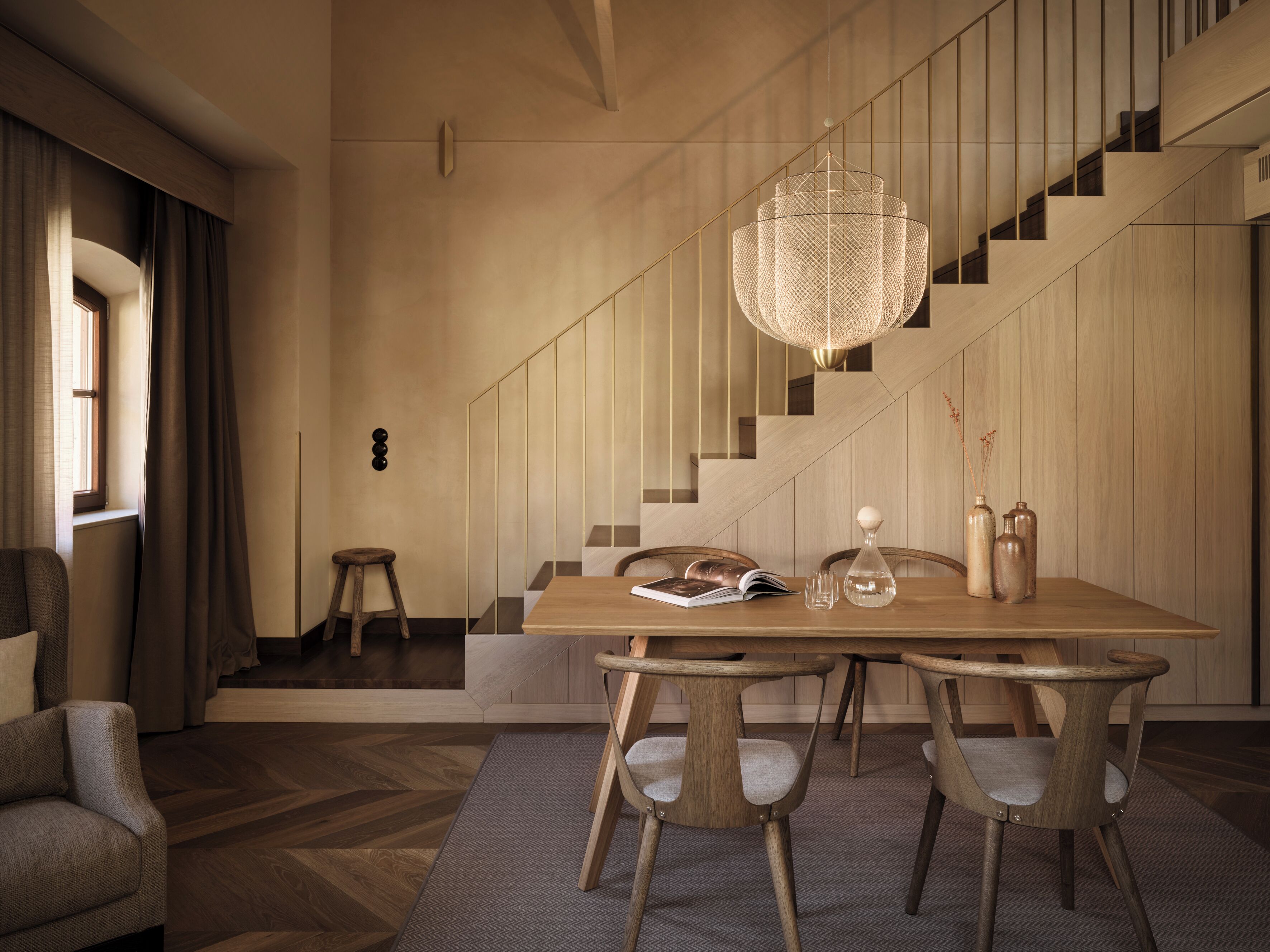 Ein moderner Essbereich mit einem Holztisch, vier Stühlen, einer hängenden Leuchte und einer Treppe im Hintergrund.
