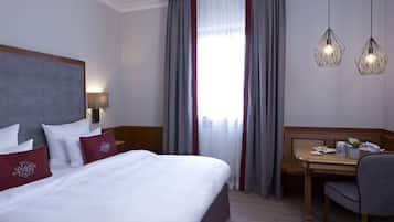 Habitación de hotel con una cama grande, un escritorio y una silla. Cuenta con una ventana con cortinas, una lámpara y dos lámparas colgantes.