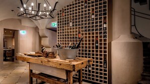 A wooden table with wine bottles and a bucket of wine glasses in a room with a wine cellar wall. - Platzl Hotel (Munich)