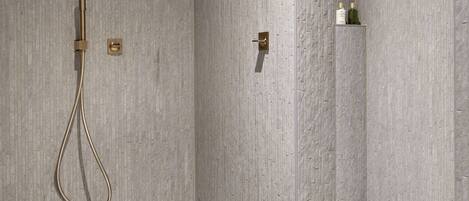 A modern bathroom with a shower, a round wooden stool with toiletries, and a minimalist design.