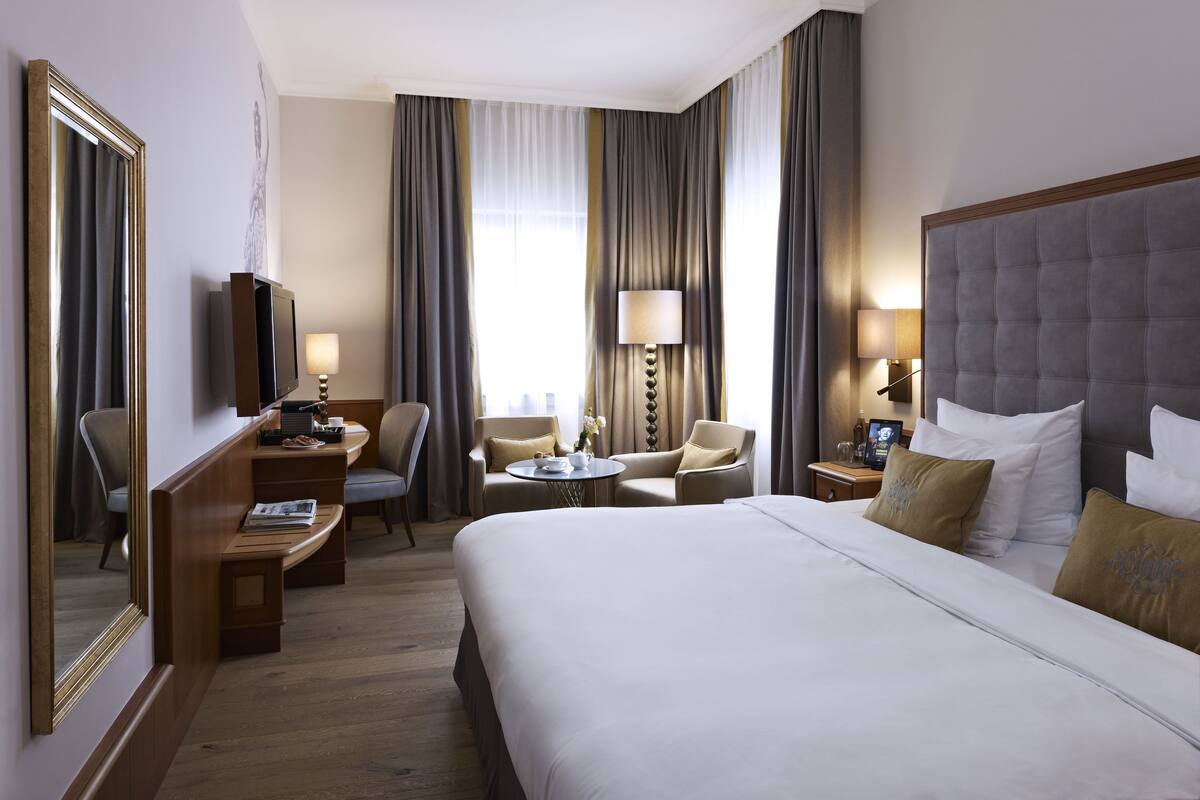 Habitación de hotel con una cama grande, un escritorio, dos sillones, un televisor y una lámpara.