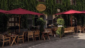 An outdoor café with wooden tables and chairs, red umbrellas, and ivy-covered walls. - Platzl Hotel (Munich)