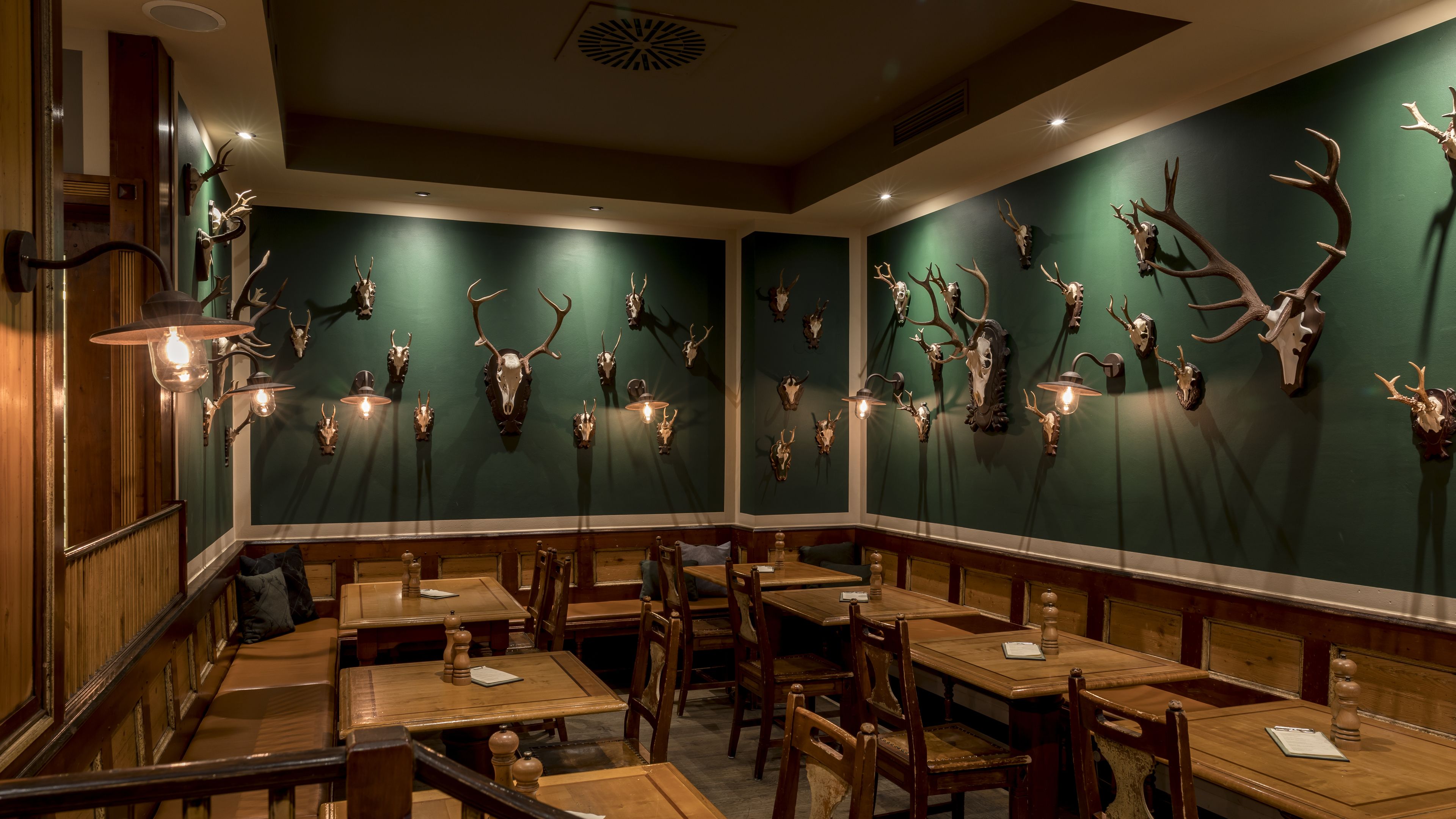 Un restaurante con mesas y sillas de madera, paredes verdes y cráneos de animales montados.