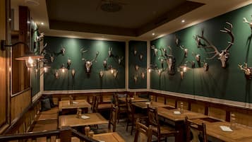 Un restaurante con mesas y sillas de madera, paredes verdes y cráneos de animales montados.