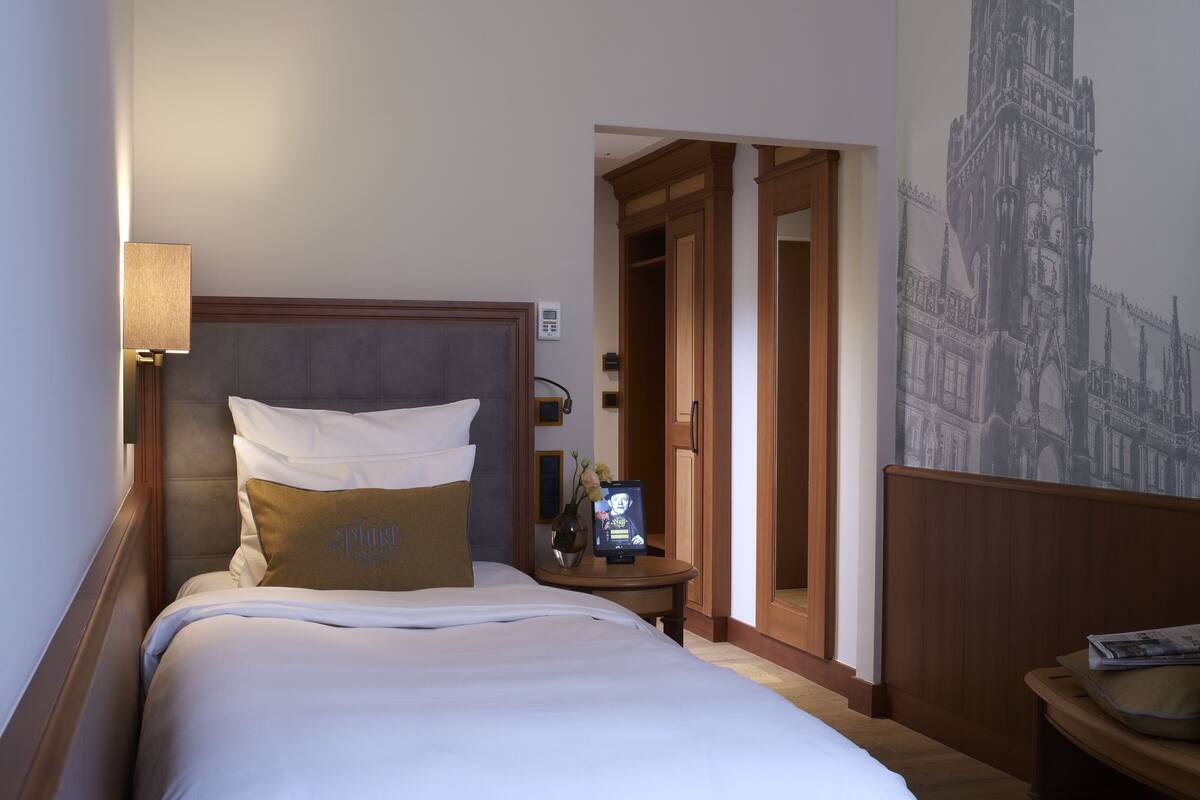 Una habitación de hotel con una cama grande, una mesita de noche, una lámpara y un reloj de pared.