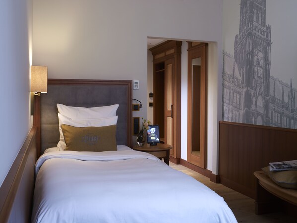 A hotel room with a large bed, a nightstand, a lamp, and a wall-mounted clock.
