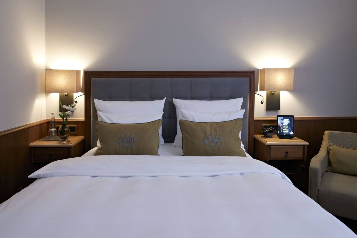 Habitación de hotel con una cama grande, dos mesitas de noche, una lámpara y una silla.