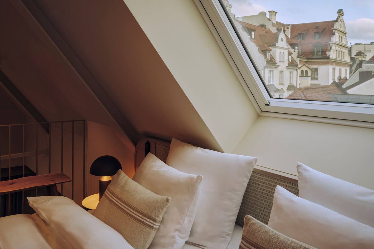 Un dormitorio con techo inclinado, un tragaluz y vistas a edificios a través de la ventana.