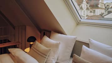 Ein Schlafzimmer mit schrägverdeckter Decke, einem Oberlicht und Blick auf Gebäude durch das Fenster.